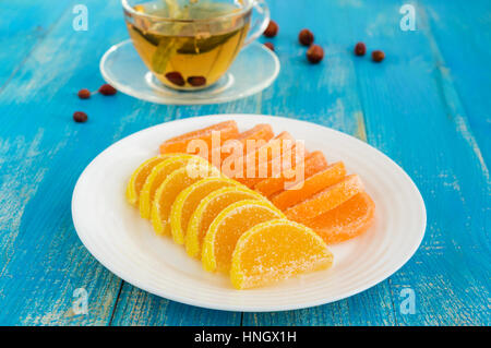 Gelee Bonbons in Form Zitrone Scheiben mit Zucker und einer Tasse Tee mit einem Linden auf blauem Grund bedeckt. Stockfoto