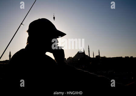 Anonyme Silhouette Mann zieht an seiner Zigarette, während Fischen auf der Galata-Brücke mit den Minaretten der Istanbul im Hintergrund. Stockfoto