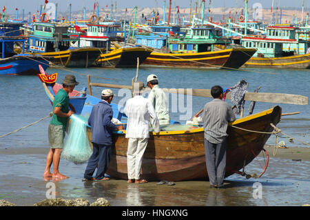 Mui Ne, Vietnam - 10. Februar 2005: Gruppe von Männern am Ufer versammeln sich um ein kleines hölzernes Boot und Angeln Materialien vorzubereiten. Mui Ne hat einen geschäftigen Fisch Stockfoto