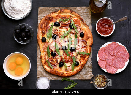 Hausgemachte Pizza und Zutaten auf dunklem Hintergrund, Ansicht von oben Stockfoto