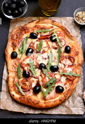 Pizza mit Tomaten, Salami und Oliven über Papier Stockfoto