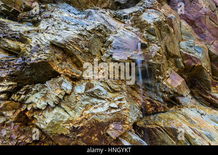 Wasser kaskadenförmig ein Mineral Reich, felsigen Klippe Gesicht. Stockfoto