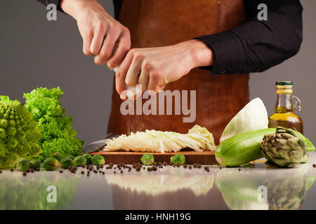 Chef kocht Gemüse mit Salz-Shaker. Sammlung von grünem Gemüse auf einer Whute Oberfläche Stockfoto