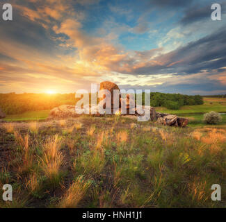 Sommer Landschaft bei Sonnenuntergang. Großen Steinen, grünen und gelben Rasen gegen bewölkter Himmel mit Sonnenlicht. Reisen und Natur Hintergrund. Felsen in der schönen Stockfoto