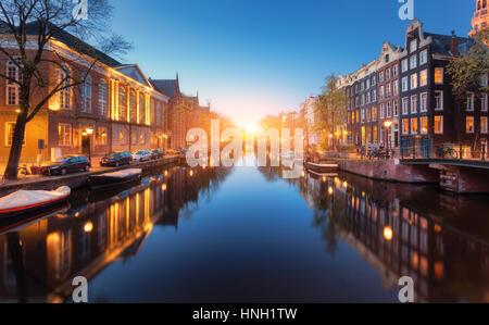 Bunte Stadtbild bei Sonnenuntergang in Amsterdam, Niederlande. Spiegelt sich die Lichter der Stadt im Wasser mit blauem Himmel in der Dämmerung. Nachtbeleuchtung von Gebäuden und Stockfoto