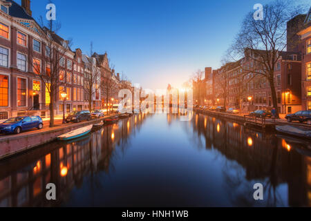 Bunte Stadtbild bei Sonnenuntergang in Amsterdam, Niederlande. Spiegelt sich die Lichter der Stadt im Wasser mit blauem Himmel in der Dämmerung. Nachtbeleuchtung von Gebäuden und Stockfoto