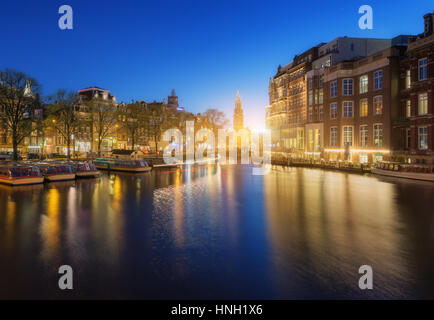 Bunte Stadtbild bei Sonnenuntergang in Amsterdam, Niederlande. Spiegelt sich die Lichter der Stadt im Wasser mit blauem Himmel in der Dämmerung. Nachtbeleuchtung von Gebäuden Stockfoto