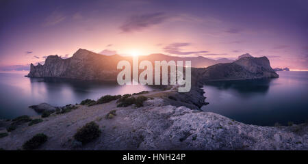 Schöne Berge gegen bunte bewölkten Himmel bei Sonnenuntergang. Landschaft mit Felsen, Meer, Gebirge, Wald, lila Himmel und Lichter der Stadt im Sommer. Na Stockfoto