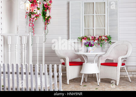 Weiße Landhaus im Provence-Stil mit Blumen geschmückt. Die Sommerresidenz und ein Ort zum Entspannen mit Korbmöbel. Stockfoto