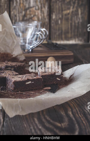 Hausgemachte dunkle Schokoladen-Brownies mit Frischkäse auf Backpapier auf rustikalen Holztisch Stockfoto