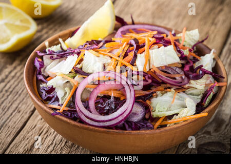 Hausgemachte wenig Kalorien Chinakohl Salat mit Rotkohl, Karotten und rote Zwiebel in Keramikschale auf rustikalen Holztisch. Gesund Vegan Food Konzept Stockfoto