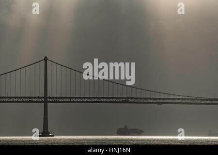 Ein Containerschiff segelt durch Nebel und Wolken unter der Oakland Bay Bridge in der San Francisco Bay Stockfoto