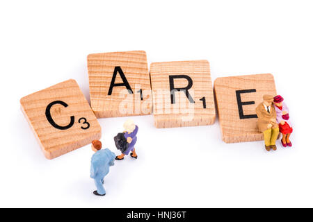 Scrabble Buchstaben bilden das Wort Pflege. Ein älteres Ehepaar sitzen auf der Buchstabe E des Wortes Pflege als ein jüngeres paar zu Fuß. Stockfoto