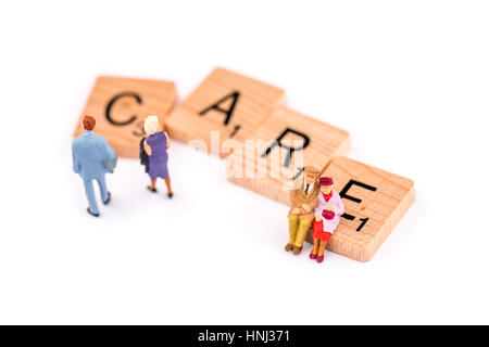 Scrabble Buchstaben bilden das Wort Pflege. Ein älteres Ehepaar sitzen auf der Buchstabe E des Wortes Pflege als ein jüngeres paar zu Fuß. Stockfoto