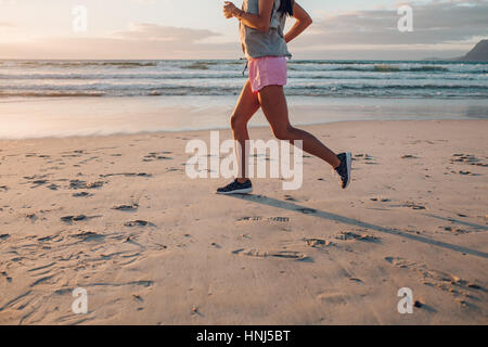 Niedrige Abschnitt Schuss von junge Frau am Strand joggen. Fitness Frauen auf Morgenlauf am Meeresufer, Fokus auf Füßen. Stockfoto