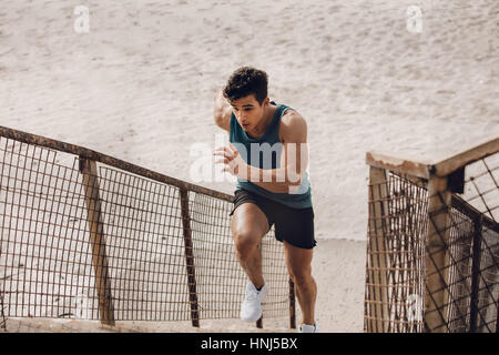 Passen Sie jungen Mann läuft die Stufen am Strand. Männliche Läufer trainieren am Strand. Stockfoto