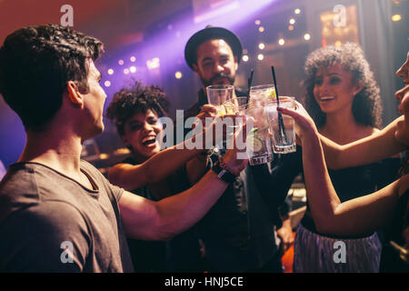 Glückliche junge Freunde in bar mit Cocktails toasten. Gruppe von Männern und Frauen im Nachtclub feiert mit Getränke. Stockfoto