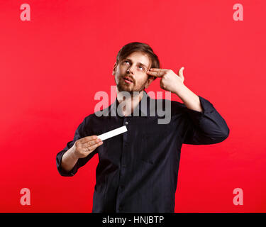 Mann hält eine leere Exemplar. Werbefläche. Ein attraktiver Mann und mit einem Schild mit beiden Händen. Er legte zwei Finger auf den Kopf mit Pistole. Stockfoto