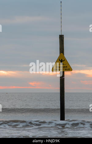 Gefahrenzeichen Versenkung Schlamm vor der Wellen und den Sonnenuntergang. Warnung vor gefährlichen Küste bei Weston-super-Mare, Somerset, UK, mit Flut Stockfoto