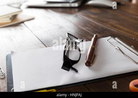 Brille, Kugelschreiber und Notizblock auf hölzernen Schreibtisch Stockfoto