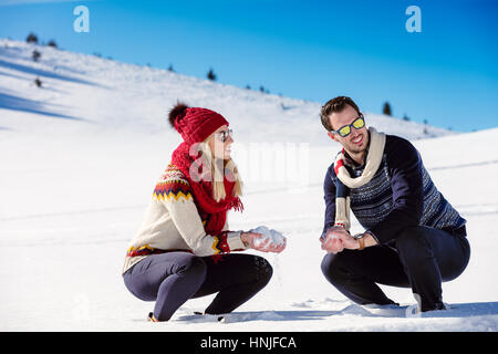 Schneeballschlacht. Winter-Paare, die Spaß im Schnee im Freien spielen. Junge fröhliche multiethnische Brautpaar. Stockfoto