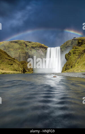 Ein Regenbogen durch Wassernebel Aus Wasserfall Skogafoss, gesehen von der Skoga River flussabwärts, Island Stockfoto