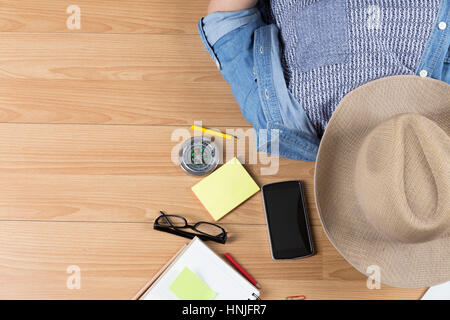 Frau liegend auf Holzboden mit Hut, Handy, Notebook und Karte Stockfoto