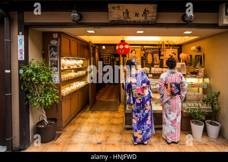 Zwei junge Hündin, die in traditionellen japanischen Kostüm, Kimono an eine Bäckerei im Stadtteil Gion, Kyoto, Japan Stockfoto