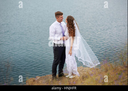 Braut und Bräutigam umarmt am See spazieren Stockfoto