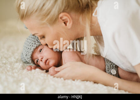 Kaukasische junge Mutter ihr neugeborenes Baby-jungen, der auf dem Bauch auf einem Bett sitzt küssen Stockfoto