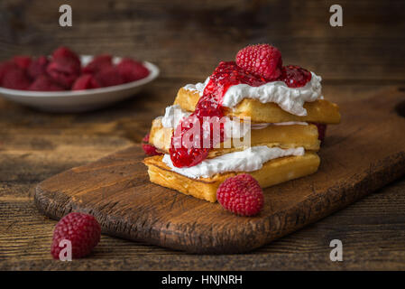 Belgische Waffeln mit Himbeeren und Sahne auf rustikalen Tisch. Stockfoto