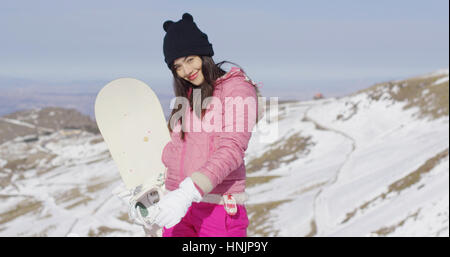 Drei Viertel Körper Porträt der lächelnde junge Asiatin mit ihrem Snowboard im verschneiten Berglandschaft. Sie genießt Winterurlaub am Hang. Stockfoto