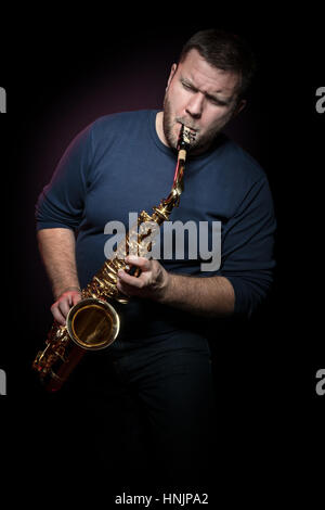 Bärtige Saxophonist mit geschlossenen Augen spielt hysterisch ein Saxophon, auf schwarzem Hintergrund isoliert Stockfoto