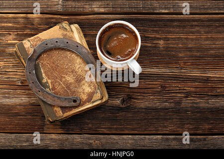 Altes Buch, rostige Hufeisen und Tasse Kaffee auf hölzernen Hintergrund mit dem leeren Raum für Text. Symbol für Glück Konzept. Stockfoto