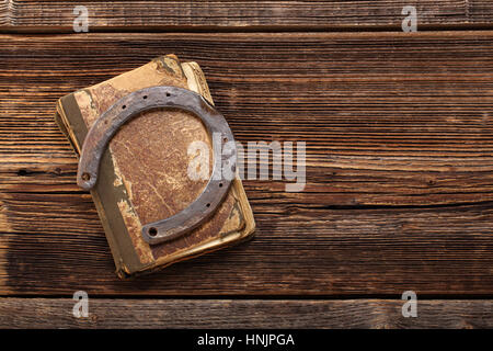 Altes Buch und rostigen Hufeisen auf hölzernen Hintergrund mit dem leeren Raum für Text. Symbol für Glück Konzept. Stockfoto