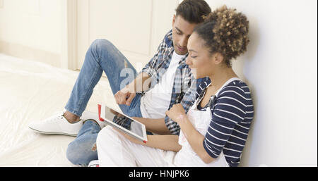 Hübsches schwarzes paar sitzt und Tablet auf Plane und gegen eine weiße Wand sitzen Stockfoto