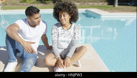 Junges Paar zum Entspannen in der Sonne an einem Pool auf der gefliesten Surround im Chat sitzen und Lächeln Stockfoto