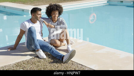 Junge Frau mit einem Afro Frisur mit ihrem Freund auf einen heißen Sommer Tag sitzen zusammen im Chat auf den gefliesten Surround am Pool entspannen Stockfoto