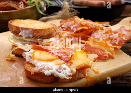 Sandwich mit Spiegelei und heißem Speck Stücke auf hölzernen Hintergrund Stockfoto