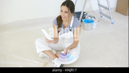 Junge Frau, die ihre neuen Farbe für das Haus zu wählen, wie sie plant, ihre Renovierung nach ihr Hab und gut in Kisten packen Stockfoto