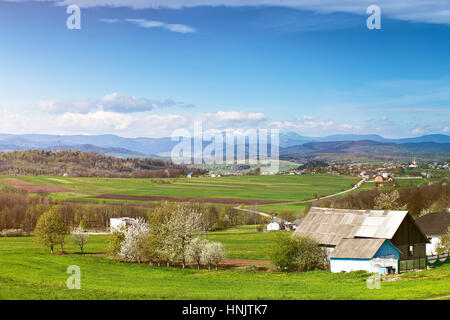 Frühling-Felder und Obstgarten blühen auf Ausläufern. Sonnigen, grünen Frühlingslandschaft. Frühling Wiesen und blühenden Bäumen. Dorf und Stadt hinter Ausläufern Stockfoto