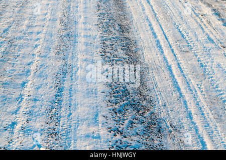 schneebedeckte Straße nach dem letzten Schneefall. Fahrbahn klein, die die Strecke und die Räder Spuren. Foto Nahaufnahme im Winter. Kleine Schärfentiefe Stockfoto