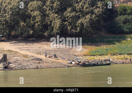 Vier Männer, die ein schweres 45 Liter Fass in einer Schlinge, die Ufer von einer Ladung Boot auf dem Irrawaddy Fluss in Mandalay (Myanmar). Stockfoto