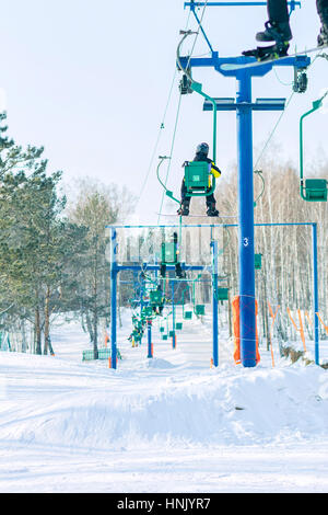 Snowboarder steigt auf dem Sessellift auf die Strecke. Stockfoto