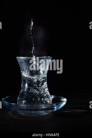 Transparente Glasschale mit Schwellen das kochende Wasser hinein. Der Dampf von oben. Schwarzer Hintergrund. Platz für Text. Stockfoto