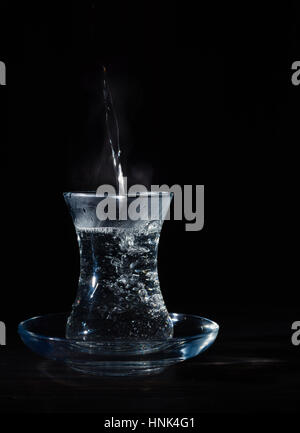 Transparente Glasschale mit Schwellen das kochende Wasser hinein. Der Dampf von oben. Schwarzer Hintergrund. Platz für Text. Stockfoto