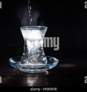 Transparente Glasschale mit Schwellen das kochende Wasser hinein. Der Dampf von oben. Schwarzer Hintergrund. Platz für Text. Stockfoto