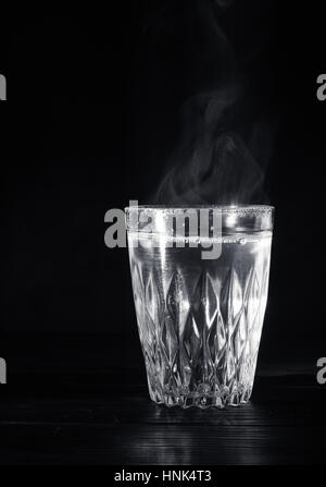 Transparente Glasschale mit Schwellen das kochende Wasser hinein. Der Dampf von oben. Schwarzer Hintergrund. Platz für Text. Stockfoto