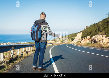 Hübscher junger Mann Tramper stehen auf einer Autobahn. Abenteuer und Tourismus-Konzept. Stockfoto