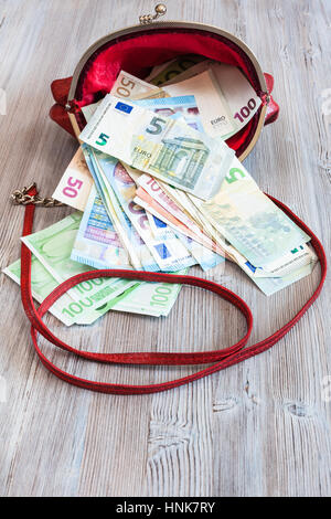 verschiedenen Euro-Banknoten Herausfallen aus rotem Lederhandtasche auf Holztisch Stockfoto